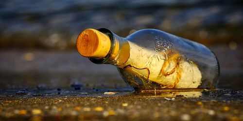 Mensaje en una botella de cristal tapada con un corcho que ha llegado a la orilla.